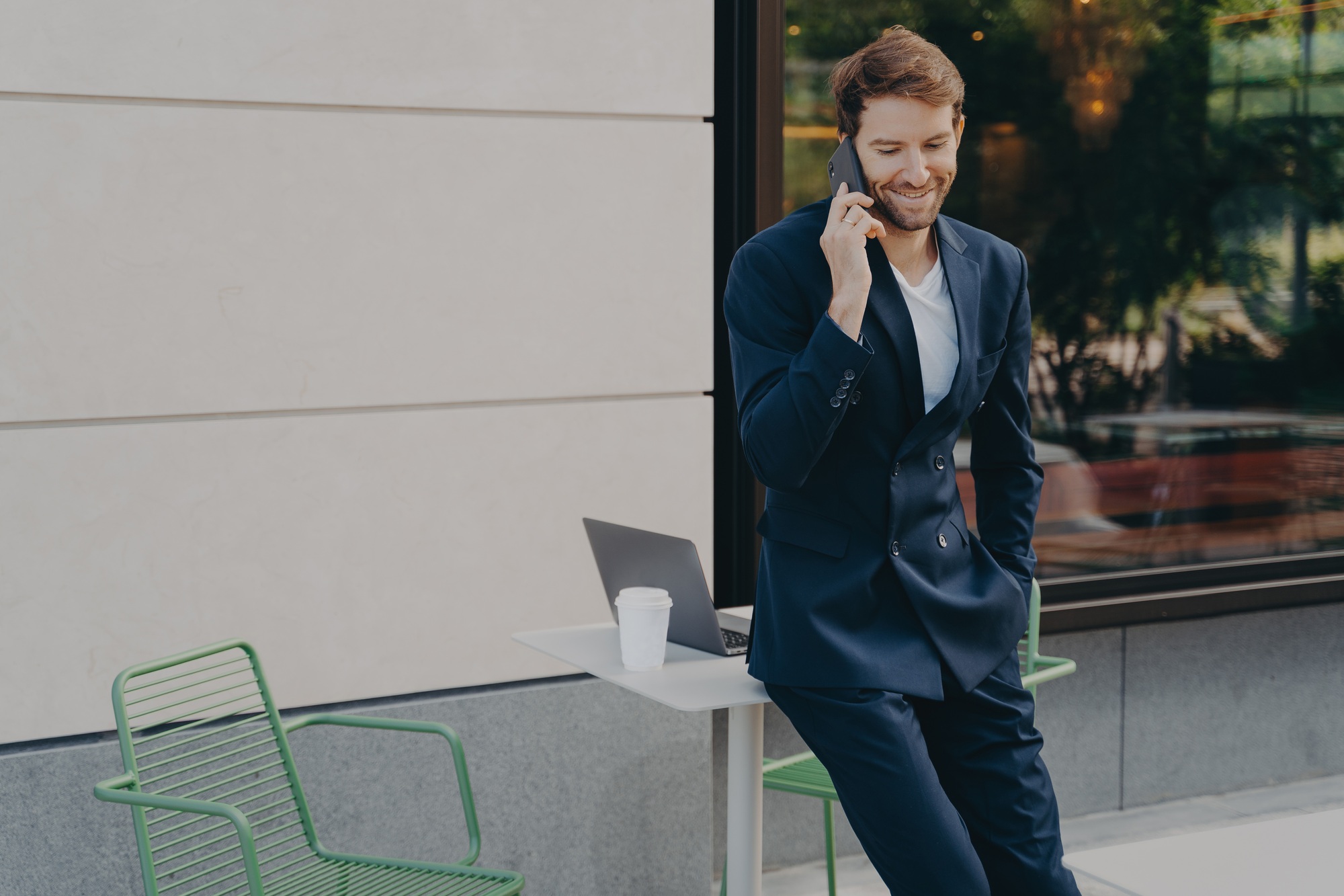 Successful handsome male trader discussing stock prices on while leaning on sidewalk cafe table