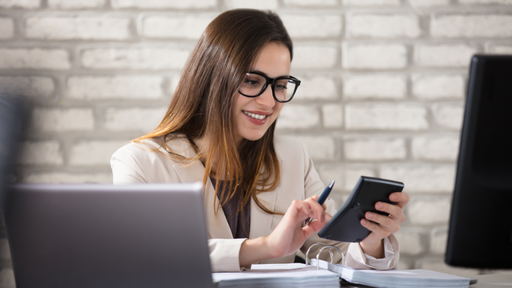 Businesswoman in office working on laptop and documents at desk.
